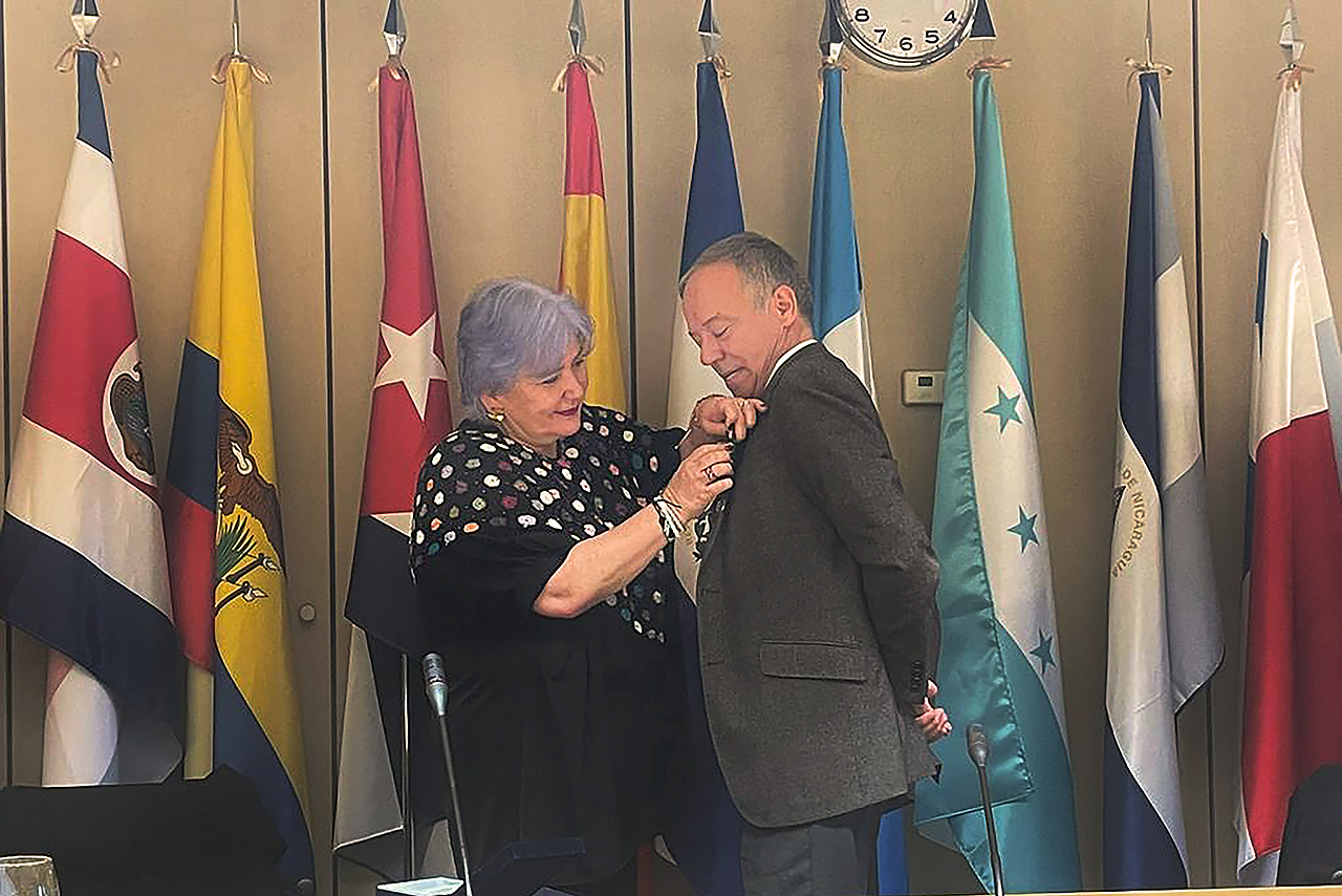 La presidenta del Parlamento Andino, Gabriela Flórez, impone la medalla al profesor Alonso