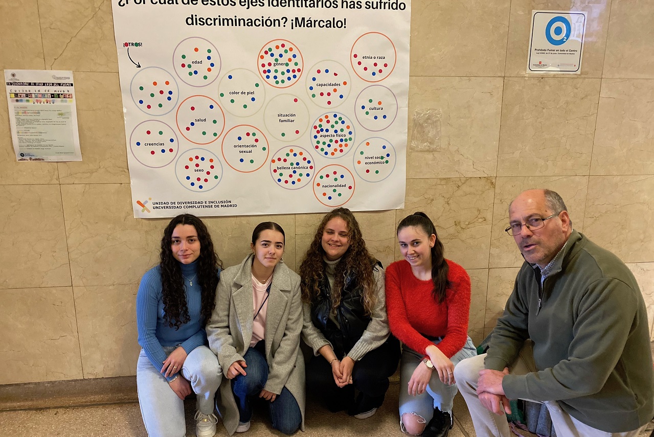El profesor Enrique Varela, de la Facultad de Enfermería, Fisioterapia y Podología, posa junto al cartel con cuatro estudiantes